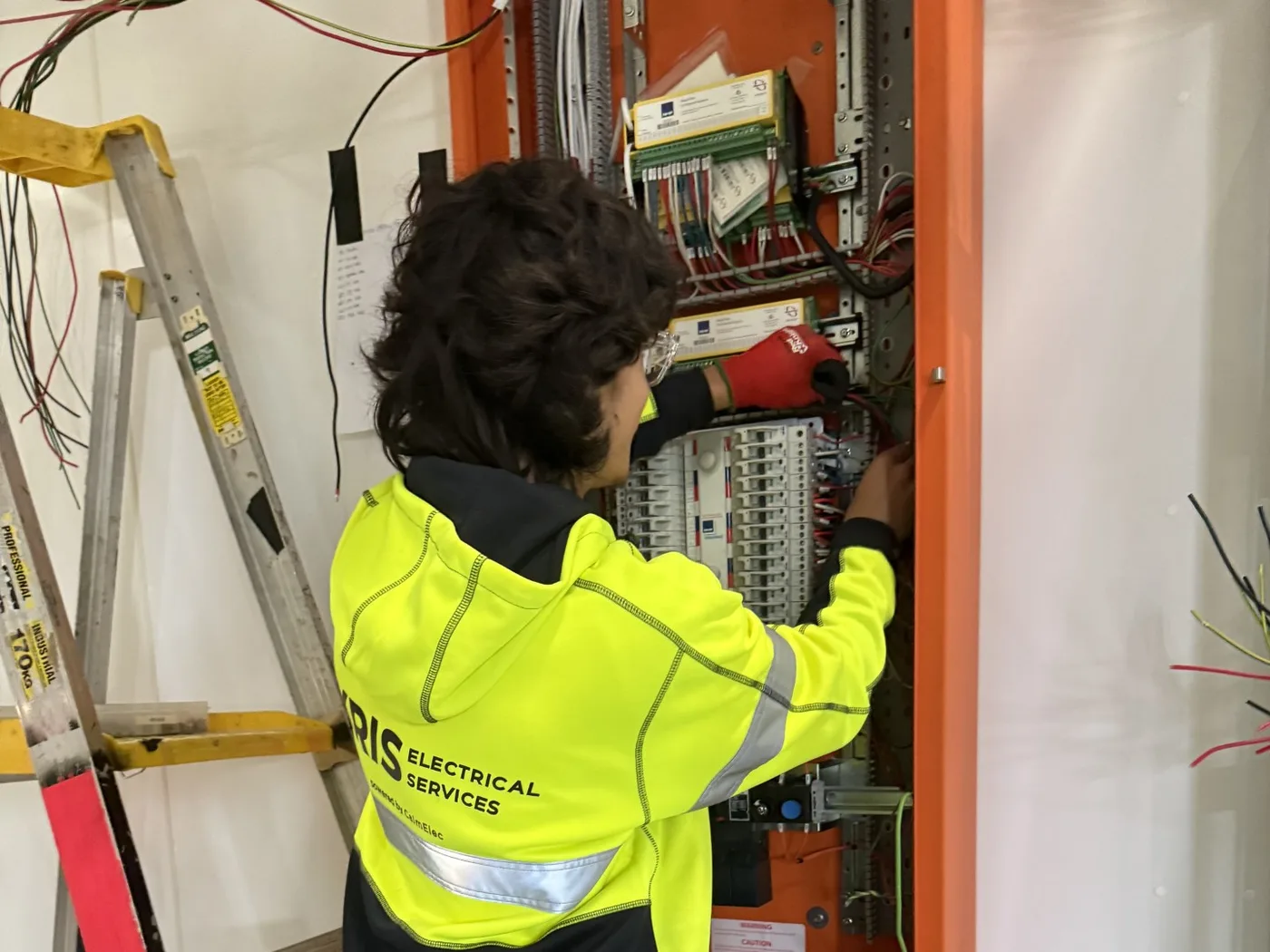 Kris Electrical Services electrician wiring circuit breakers inside an orange distribution board in a modular building