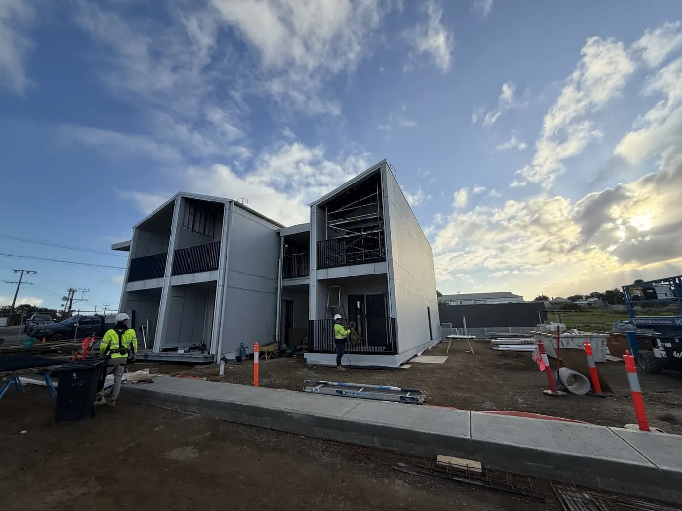 Modular building units being craned into place on a construction site with electricians in hi-vis working alongside