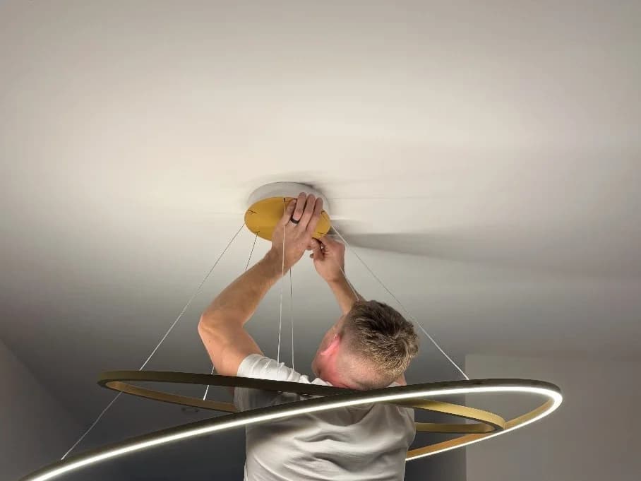An electrician on a platform fitting a large circular pendant light to a ceiling