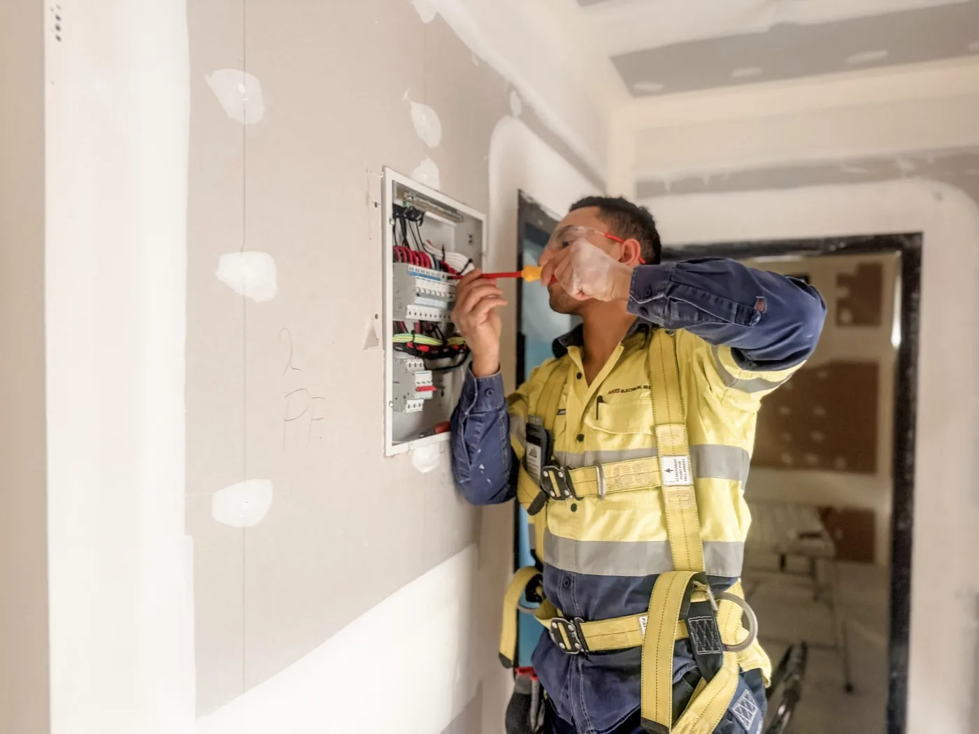 Kris Electrical Services electrician in a safety harness terminating circuit breakers in a switchboard during a new build