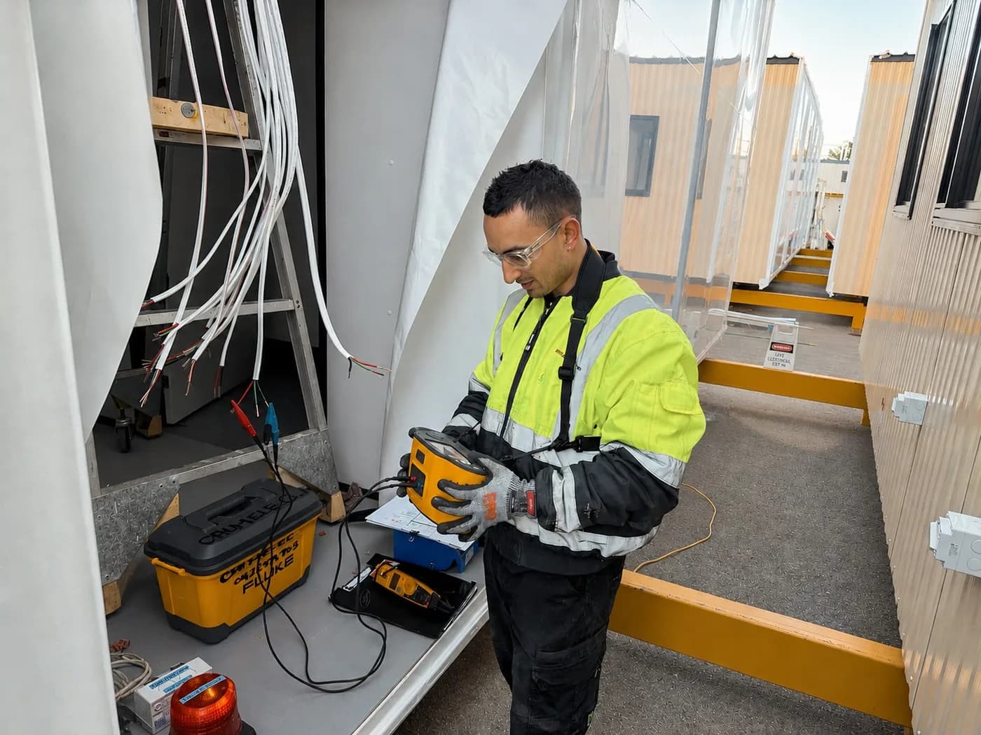 Kris Electrical Services electrician using a test instrument on the wiring of a modular building unit