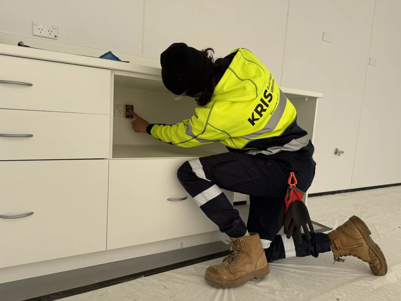Kris Electrical Services electrician kneeling at new white joinery fitting off power outlets on a commercial fit-out