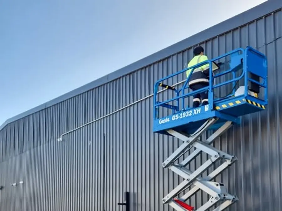 Kris Electrical Services electrician on an electric scissor lift installing external lighting on a commercial warehouse wall